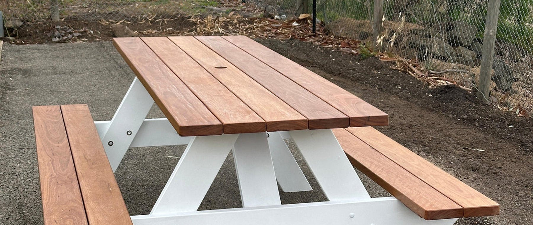 Australian hardwood picnic table with white A-frame legs and chain link fence background